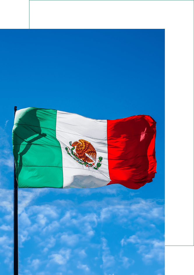 A mexican flag flying in the sky on a sunny day.